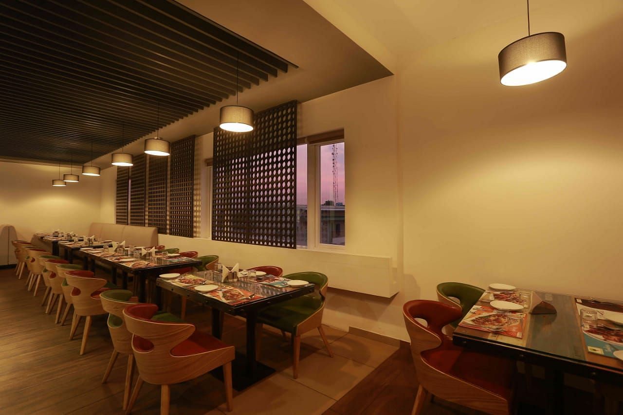 Mint N Mustard Restaurant at Mayberry Tiruppur with tables and chairs arranged neatly with hanging lights overhead